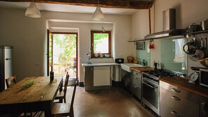 Cozinha compacta com mesa e cadeiras de madeira, forno embutido e janela com vista para áreas verdes.