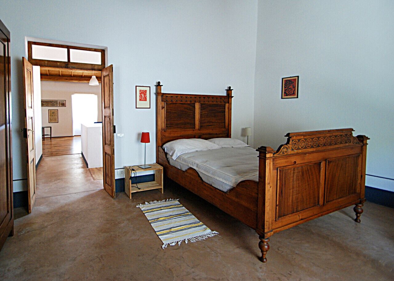 A bedroom with a wooden bed, a nightstand, a lamp, and a door leading to another room.
