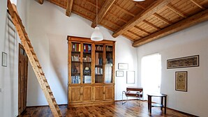 Um quarto amplo com piso de madeira, uma grande estante de madeira, um banco, uma pequena mesa e uma escada.