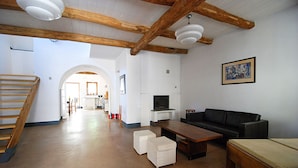 Uma sala ampla com escada de madeira, um sofá preto, uma mesa de centro de madeira e uma televisão.