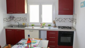 Uma cozinha compacta com armários vermelhos, fogão a gás, lava-louças e janela que traz luz natural.