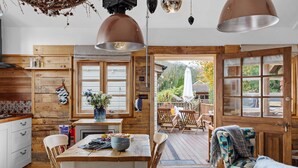 Una cocina acogedora con paredes de madera, una mesa de comedor con sillas y vistas al jardín a través de puertas abiertas.