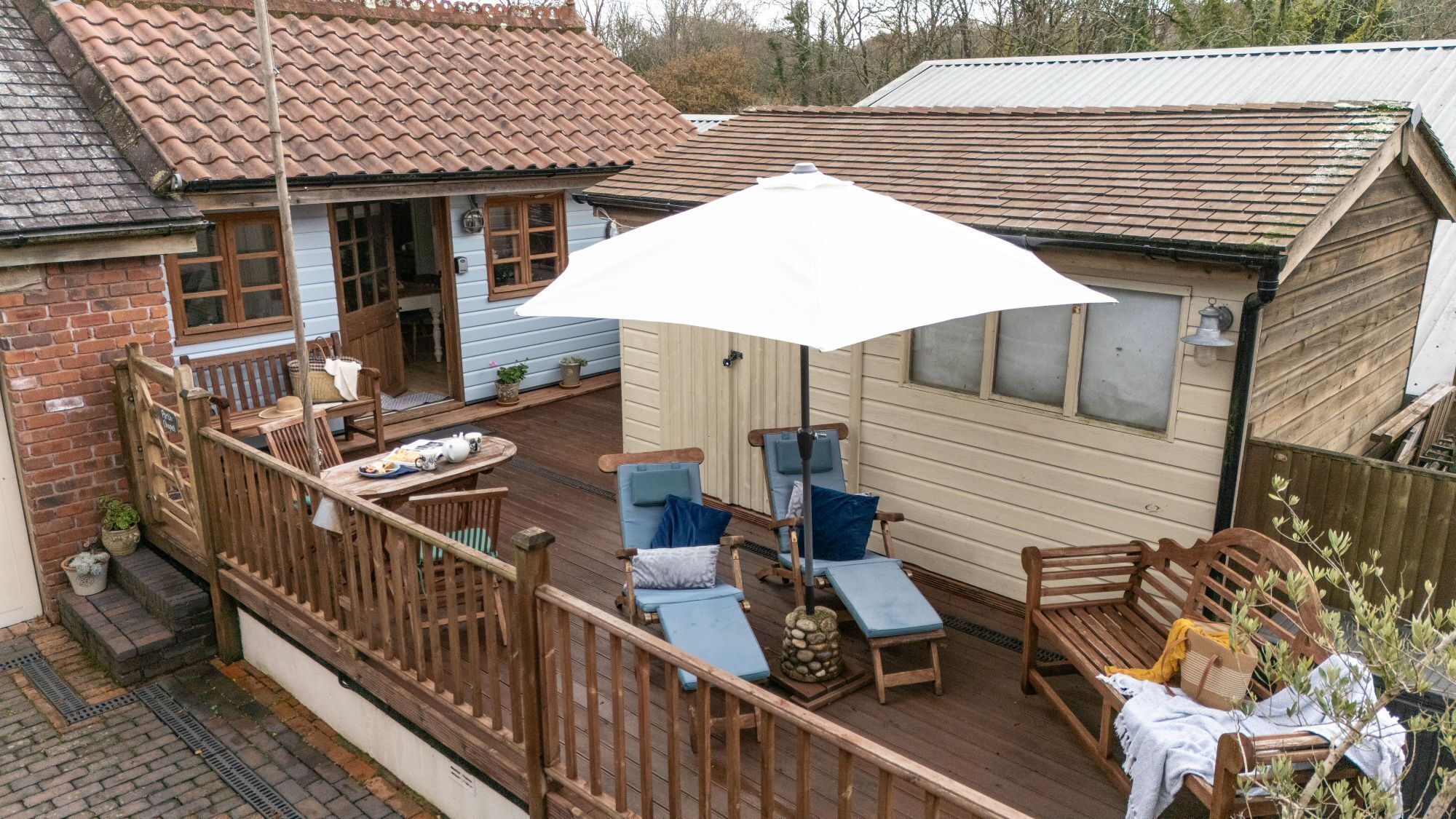 A wooden deck with outdoor seating, a white umbrella, and a house with a tiled roof.