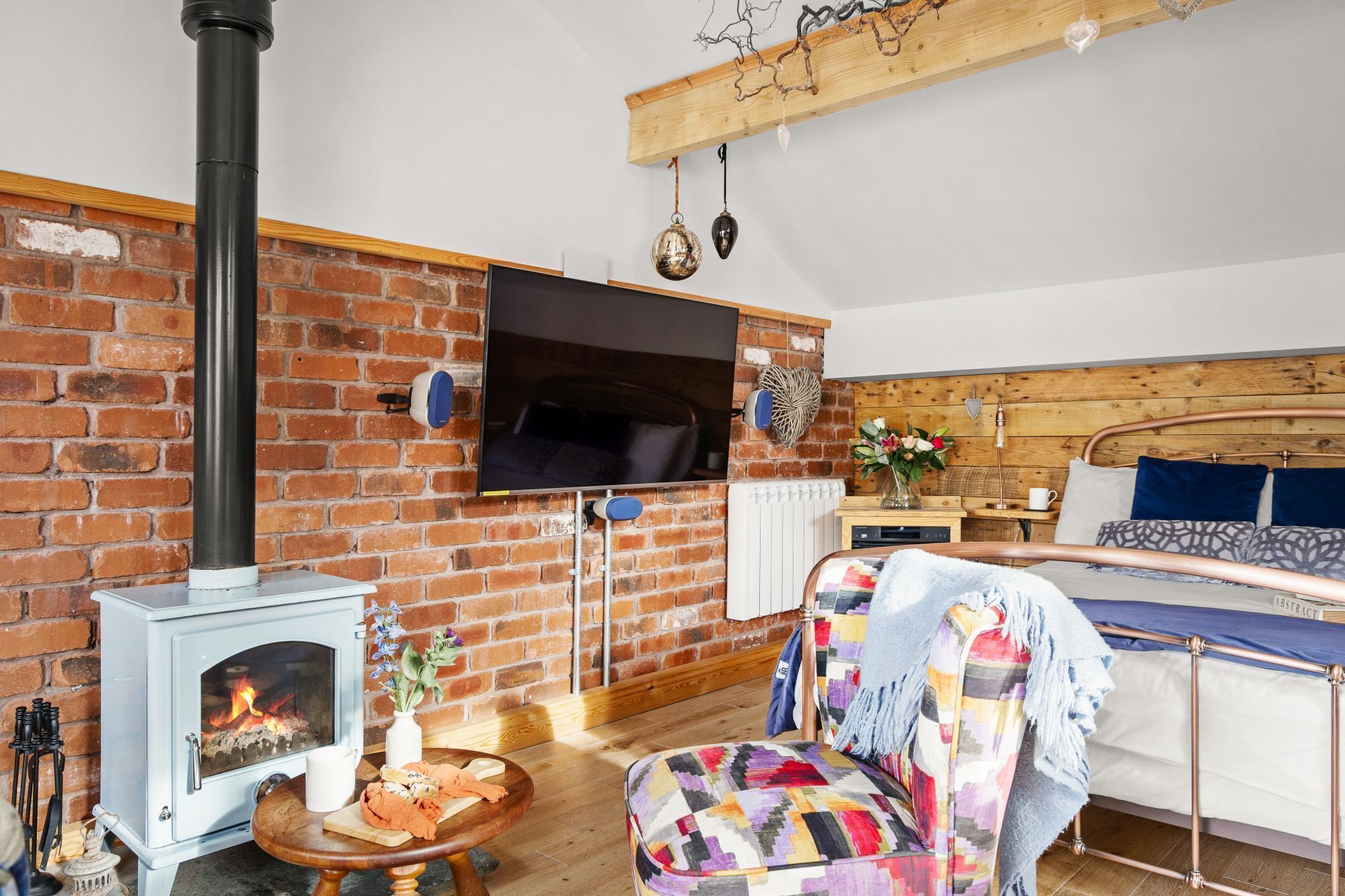 A cozy room with a brick wall, a fireplace, a bed, and a television mounted on the wall.
