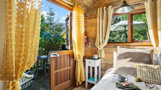 A cozy room with wooden walls, a bed with pillows, a bedside table with a lamp, and a window with curtains. - Poldhu -  Pet Friendly - Free parking and WiFi (Buryas Bridge)