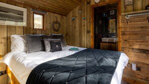Un dormitorio de cabaña de madera con una cama, un aparador, un espejo y una ventana.