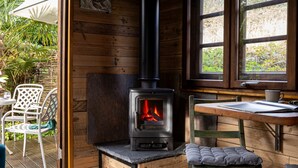 Interior acogedor de una cabaña con estufa de leña, paredes de madera, una ventana y una mesa con una taza.