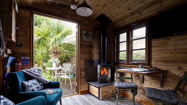 Interior acogedor de una cabaña con chimenea, paredes de madera, zona de comedor y sala de estar con un sofá y sillones azules.