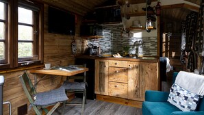 Interior acogedor de una cabaña, con paredes de madera, una zona de cocina con salpicadero de azulejos y un rincón de estar con un sofá azul.