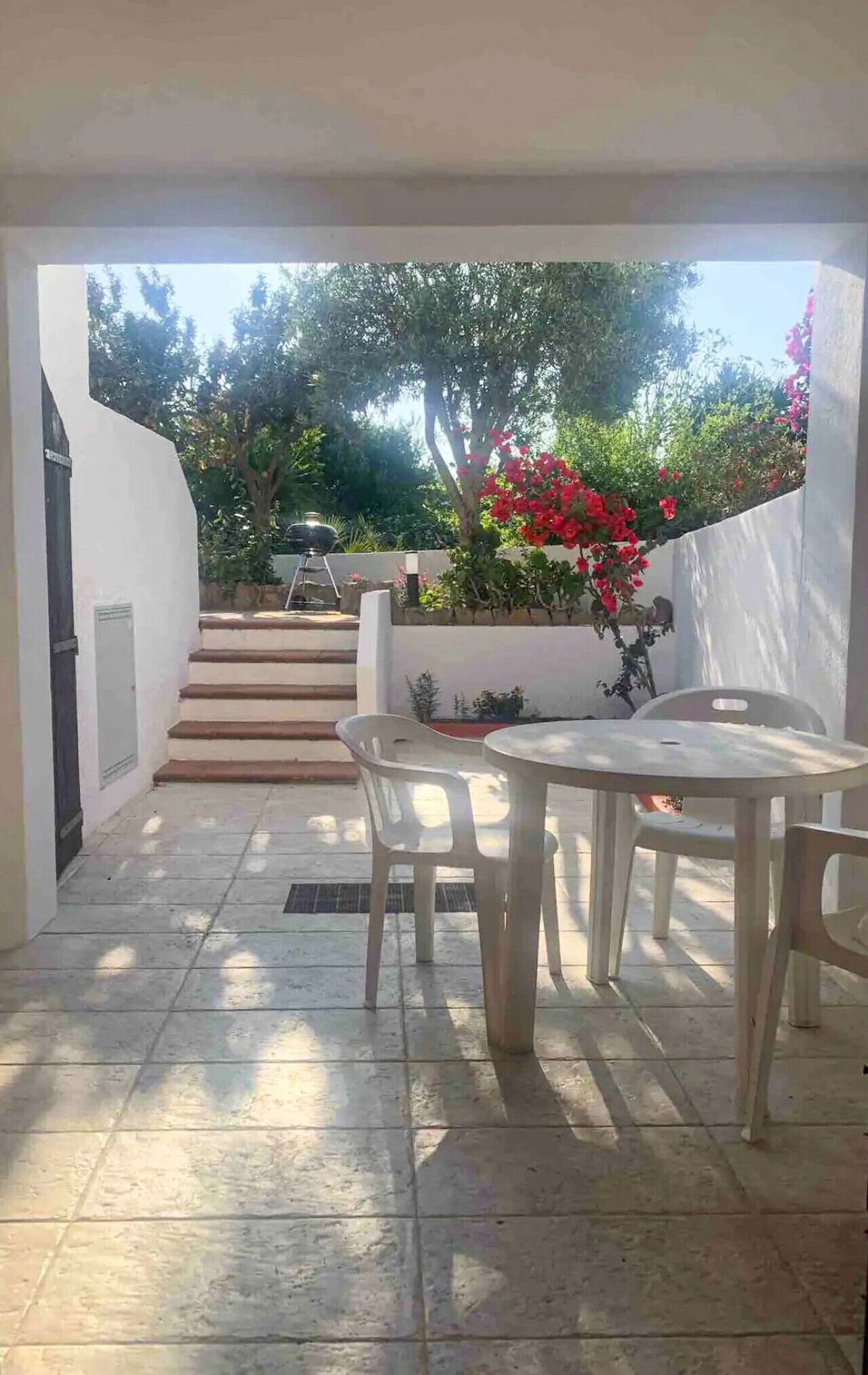 Un espace patio avec une table et des chaises, un escalier menant à un jardin et un barbecue fixé au mur.