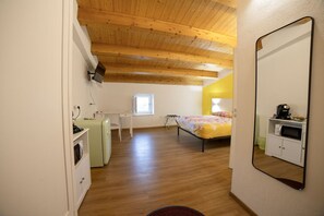 Un dormitorio pequeño con techo de madera, una cama con colcha estampada, un escritorio pequeño, un armario blanco y un microondas empotrado.