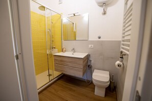 Un baño con cabina de ducha de vidrio, tocador de madera, inodoro blanco y perchero para toallas.