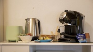 Een keukentafel met een koffiezetapparaat, een waterkoker, een fruitschaal en een koffiepads.