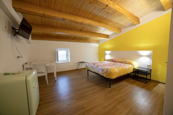 Un dormitorio con cama, escritorio, silla, mesita, lámpara y ventana.