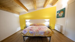 Een slaapkamer met een bed, houten vloer, een geel accentmuur en een schilderij.