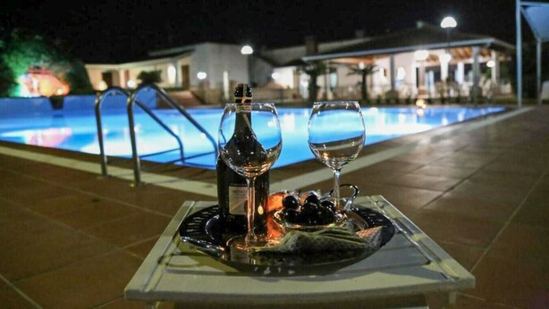 Taula amb una ampolla de vi, dues copes i un plat d'olives al costat d'una piscina de nit.