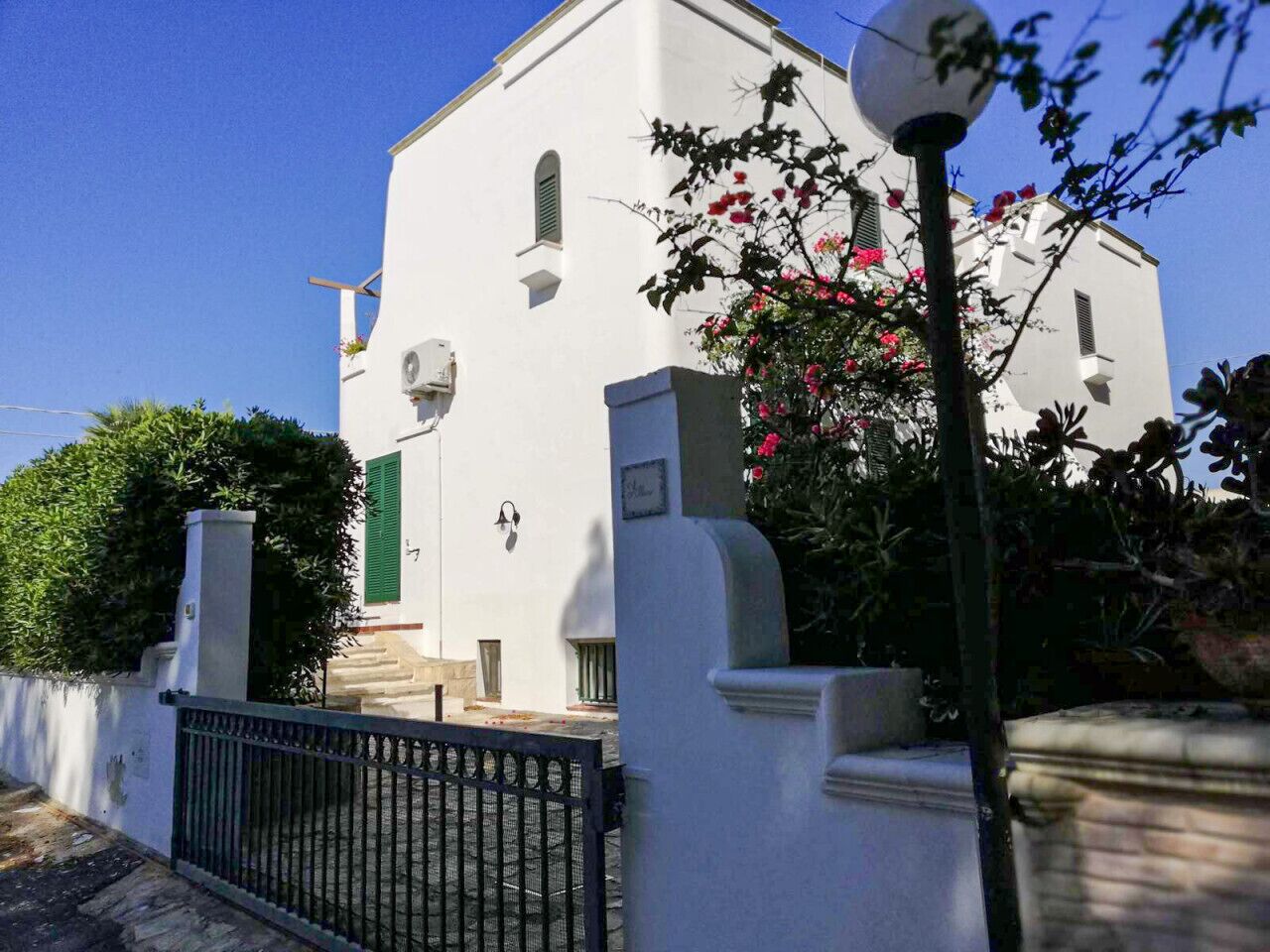 Un bâtiment blanc avec une porte verte, un portail noir et un lampadaire.