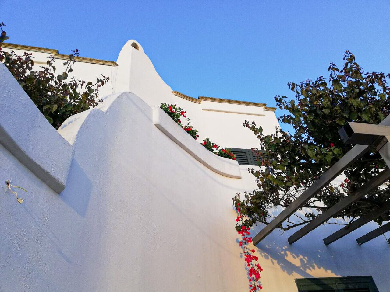 A white building with a curved roof and a small balcony with red flowers.