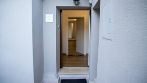 A narrow hallway with a wooden door at the end, a small rug on the floor, and a wall-mounted light fixture. - Casa Anele - Morano Calabro (Morano Calabro)