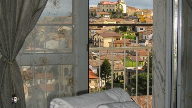Ein Bett mit Blick auf eine Stadt durch ein Fenster mit Vorhängen.