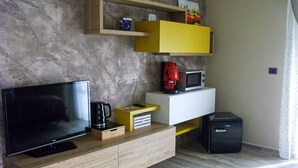 Ein modernes Wohnzimmer mit Flachbildfernseher, Kaffeemaschine, Mikrowelle und einem schwarzen Koffer auf einem Holzkabinett.