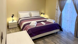 Ein Hotelzimmer mit einem Bett, zwei Nachttischen, einem Schreibtisch und einem Fenster mit Vorhängen.