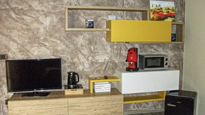 Ein modernes Wohnzimmer mit Fernseher, Kaffeemaschine, Mikrowelle und kleinem Kühlschrank.