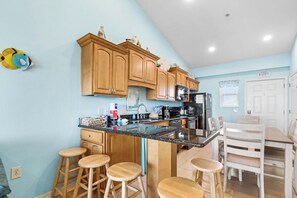 A kitchen with wooden cabinets, a granite countertop, and bar stools. - 🌞🌴Baywatch G9 | Water Views + Walk to Beach | Handicap Accessible (Pensacola Beach)