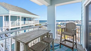 Een balkon met een houten tafel en stoelen, met uitzicht op een strandlocatie met meerdere gebouwen.