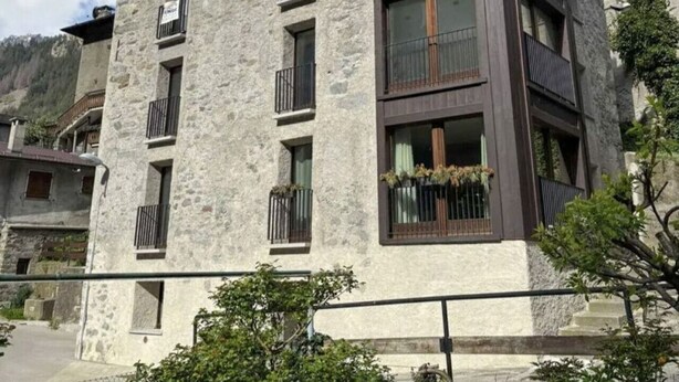 En bygning med flere etager, balkoner, en murstensfacade og et bjergrigt baggrundsmotiv.