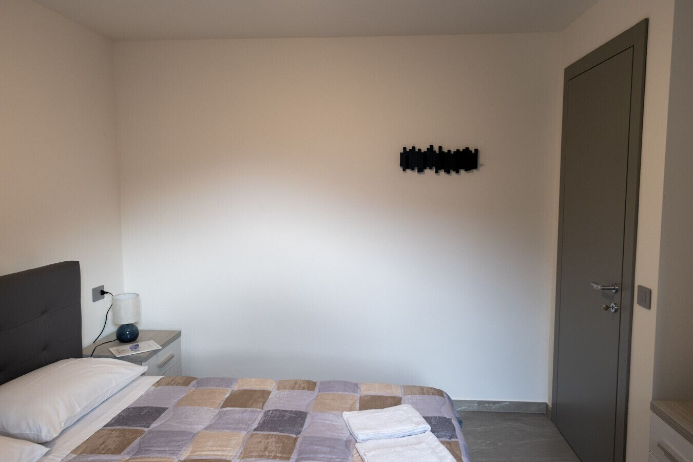 A bedroom with a bed, a nightstand, a lamp, and a door.