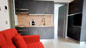 Et moderne køkken med mørke skabe, en træbordplade, og en rød sofa i forgrunden.