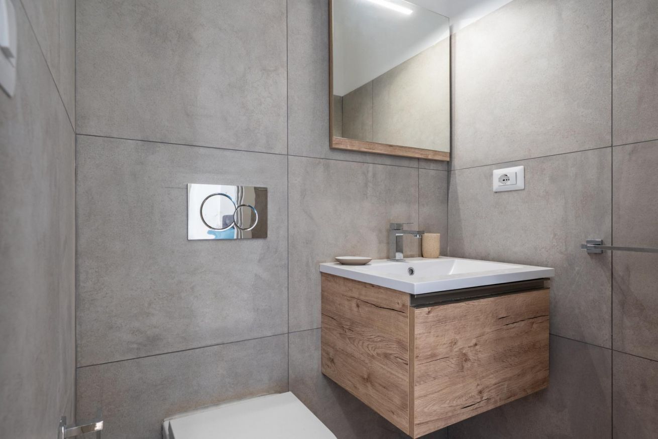 A modern bathroom with a wooden vanity, a mirror, and a toilet.