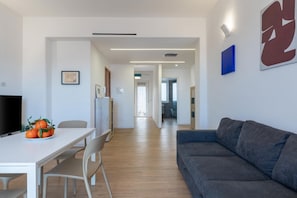 A modern living room with a sofa, a dining table with chairs, and a television. - GuestHost - Spacious and bright apartment of approximately 90 sqm, accommodating four people, located on the sixth floor of a building with an elevator (NOT wheelchair accessible).The property is located in a residential area of ​​Catania, equipped w (Catania)