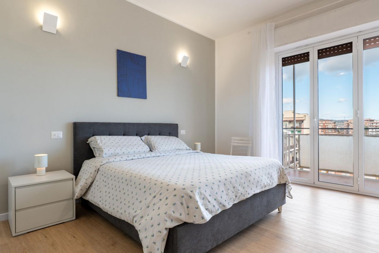 Un dormitorio con cama, mesitas de noche, un ventanal y una obra de arte en la pared.