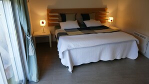 Un lit bien fait, recouvert d’une courtepointe, deux tables de chevet avec des lampes et une fenêtre avec des rideaux.