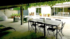 Une terrasse extérieure avec une table et des chaises, entourée de plantes en pot et dotée d’un espace abrité.