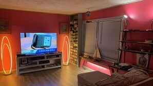 Uma sala de estar com televisão, estantes, sofá e janela com persianas.