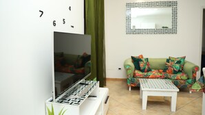 A living room with a flat-screen TV, a patterned wall clock, a green sofa, and a white coffee table. - La casetta sul mare (San Lucido)