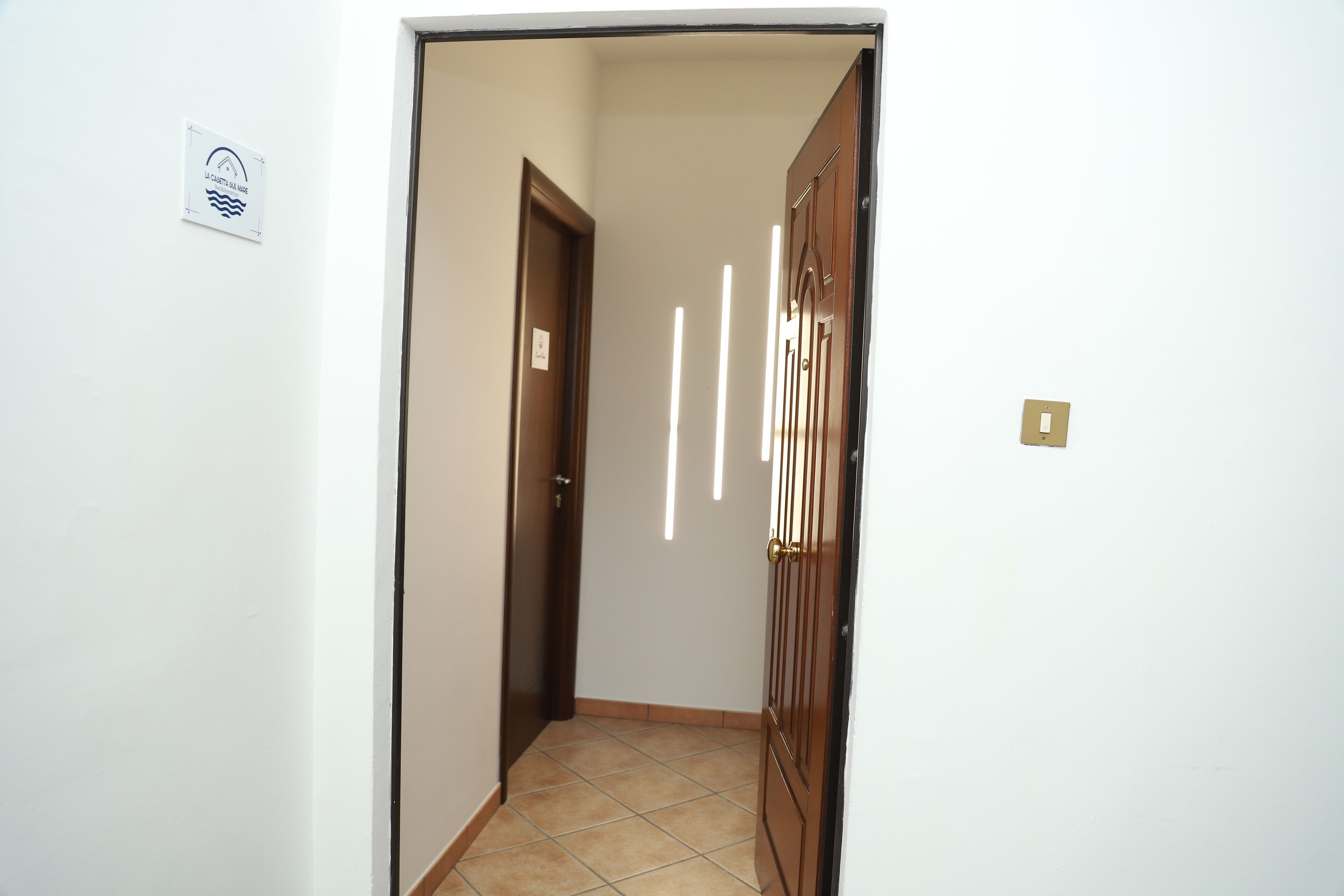 A narrow hallway with a wooden door on the right and a white wall with a sign on the left.