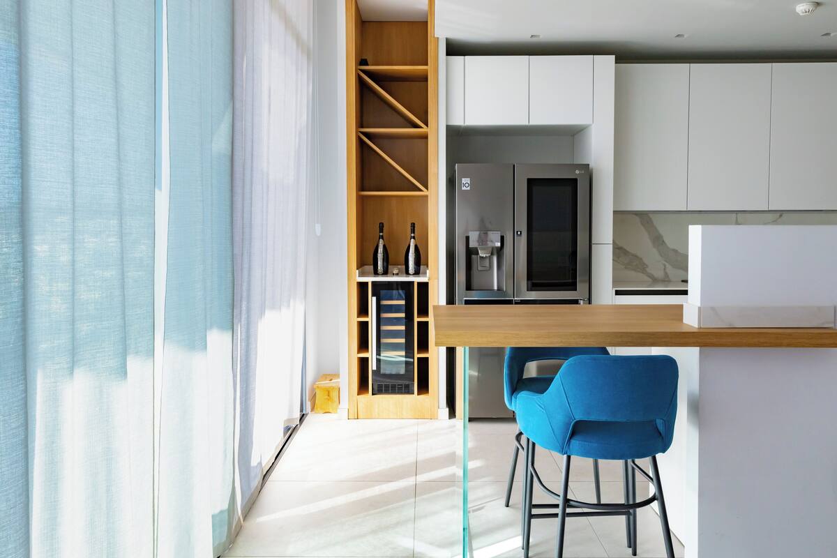 A modern kitchen with white cabinets, a built-in wine cooler, and a blue chair.