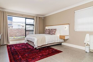 Ein Schlafzimmer mit einem Bett, einem roten Teppich, einem Fenster mit Vorhängen und Blick auf Gebäude.