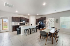 A modern kitchen with dark wooden cabinets, a central island with bar stools, a dining table with chairs, and a large refrigerator. - Stylish 4BR Escape • Open Layout • Smart TVs B (Socorro)