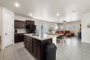 A spacious kitchen with dark wooden cabinets, a large island with a sink, and a dining area with a table and chairs. - Stylish 4BR Escape • Open Layout • Smart TVs B (Socorro)