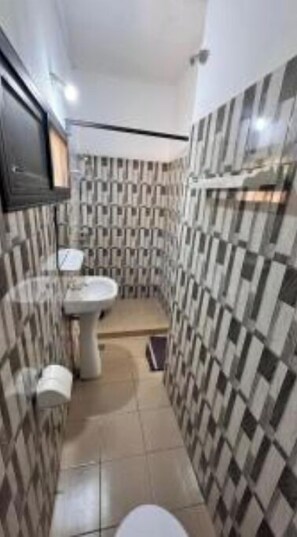 Een kleine badkamer met toilet, wastafel en spiegel. De wandtegels hebben een ruitpatroon.