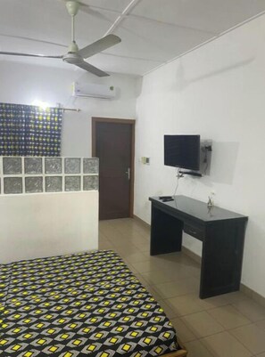 Een slaapkamer met een bed, een bureau, een televisie en een plafondventilator.