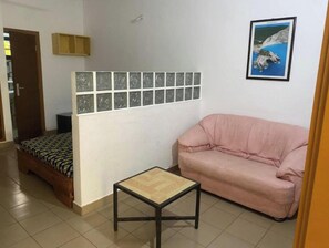Una habitación con una cama, un sofá rosa, una pequeña mesa y una pared con un diseño decorativo de azulejos.