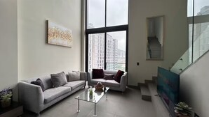 Un soggiorno moderno con un divano grigio, un tavolino in vetro e un'ampia finestra con vista sulla città.