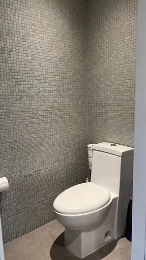 Kylpyhuone, jossa on wc, laatoitettu seinä ja wc-paperiteline.