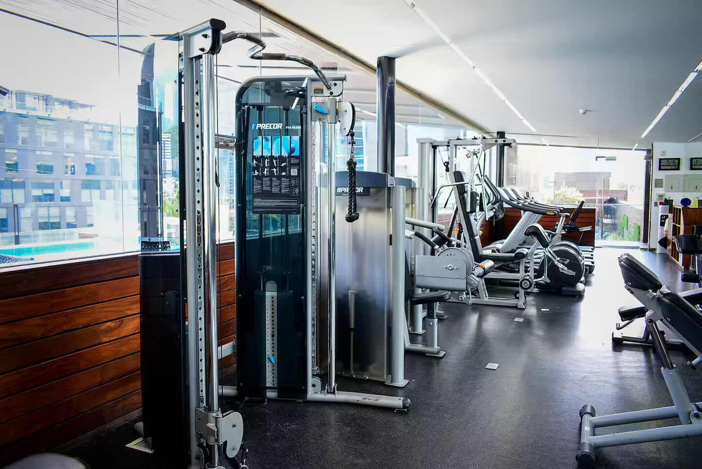 A modern gym with various exercise machines, large windows, and a clean, polished floor.